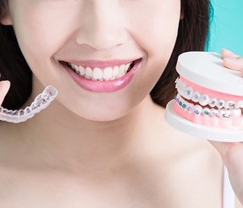 Woman holding clear aligners and metal braces