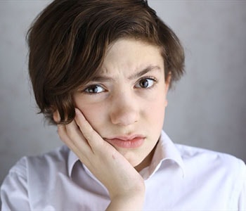 young boy patient holding his cheek in pain