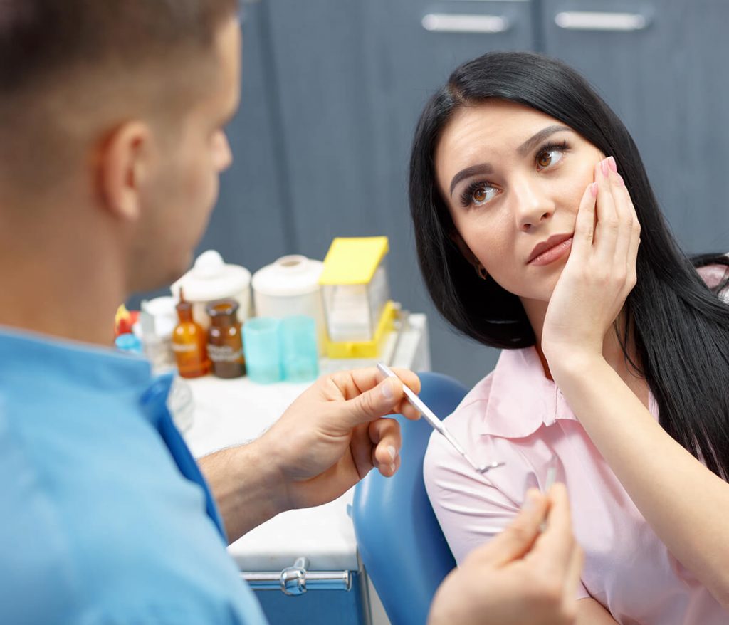 Female patient holding her cheek and talking to male dentist