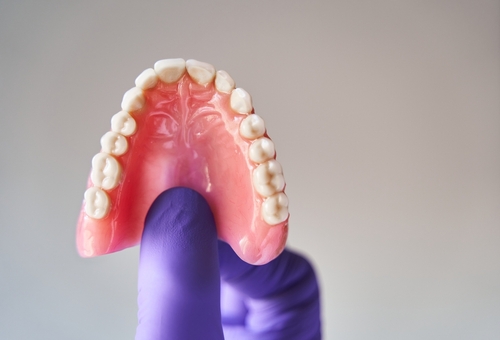 Fingers,In,Purple,Gloves,Holding,Set,Of,Dentures.